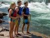 The Rafter’s Code: Inside Private Boater Culture Three private rafters, two men and a woman, stand on a sunny riverbank with throw ropes, setting safety for an upcoming rapid.
