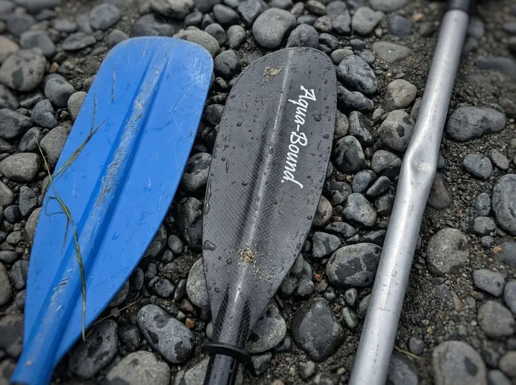 Close-up comparing fiberglass and aluminum raft paddle blades on wet rock
