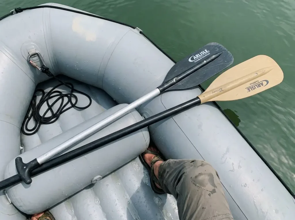 Two Carlisle raft paddles of different lengths laid across a raft tube showing guest versus stern sizing