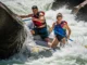 River Pinning Explained: Causes, Types & Rescue Protocol A full-body shot of a man and woman in a raft pinned sideways against a large rock in turbulent whitewater.