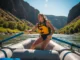 The Anatomy of an Oar Stroke: A Guide for Rafters A fit young woman in a one-piece swimsuit and life jacket expertly rowing a whitewater raft down a sunny river.