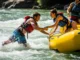 Get Back in a Raft: A Guide to Self-Rescue Techniques A fit man in his late 20s wearing a life jacket and boardshorts pulls himself back into a whitewater raft as a woman in a bikini and life jacket assists him.