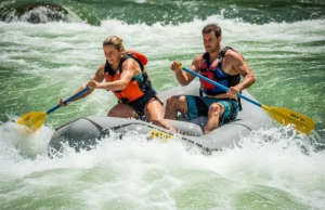 Rafting Holes: Master Speed, Angle & Power to Punch Through A man and woman in a whitewater raft paddle hard to punch through a large, splashing river hole under bright sunlight.