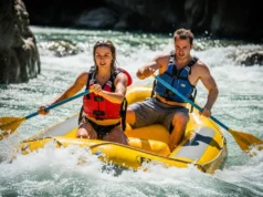 Rafting Paddle Length Explained: A Pro Rafter’s Analysis A fit young couple in a full-body view, paddling a whitewater raft through exciting rapids on a sunny day.