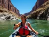 Rafting Alone: The Definitive Safety & Solo Trip Guide A full-body shot of a fit woman in her late 20s wearing a bikini and a life jacket, paddling a solo raft on a sunny day in a remote river canyon.