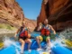 Best USA Rafting Trips: Expert-Graded by Skill & Season A fit young couple in their late 20s paddle a raft together through exciting rapids in a sunny, expansive American river canyon.