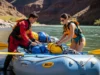 Wetsuit vs Drysuit for Rafting: A Data-Driven Guide A man in a drysuit and a woman in a one-piece swimsuit prepare their gear on a whitewater raft on a sunny day.