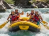 Whitewater Rafting Explained: From Rapids to River Safety A full-body shot of a group of four young adults in a raft, paddling energetically through a whitewater rapid on a sunny day