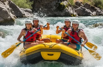 Whitewater Rafting Explained: From Rapids to River Safety A full-body shot of a group of four young adults in a raft, paddling energetically through a whitewater rapid on a sunny day