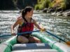 How to Row a Raft: Master Technique & Read the River A full-body shot of a fit young woman in a bikini and life jacket skillfully rowing a large raft down a sunny river.