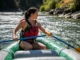 How to Row a Raft: Master Technique & Read the River A full-body shot of a fit young woman in a bikini and life jacket skillfully rowing a large raft down a sunny river.