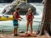 Z-Drag Rescue System: A Rafter’s Essential Safety Guide A man and woman in PFDs on a riverbank rigging a Z-drag rope system to rescue a pinned raft in the background.