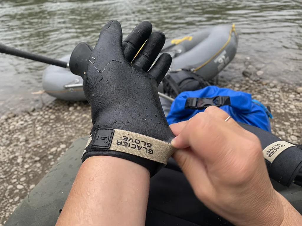 Hands pulling on a neoprene rafting glove to check the second-skin fit at the put-in