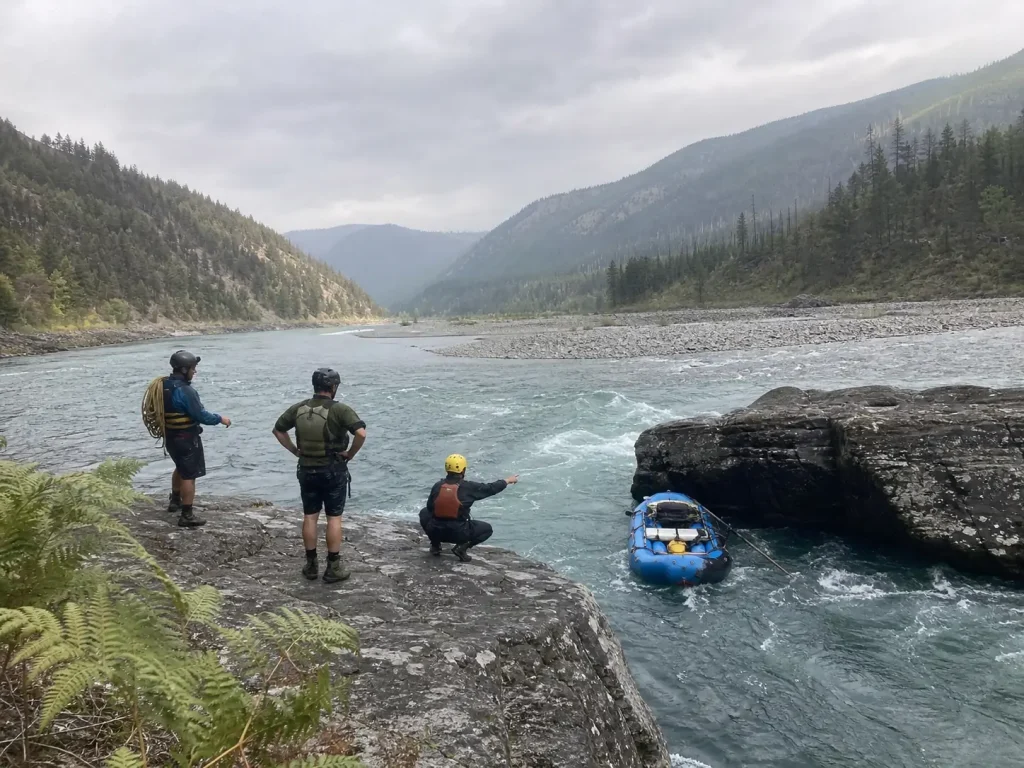 Boaters standing on a rock reading a pinned raft before rigging a mechanical advantage system