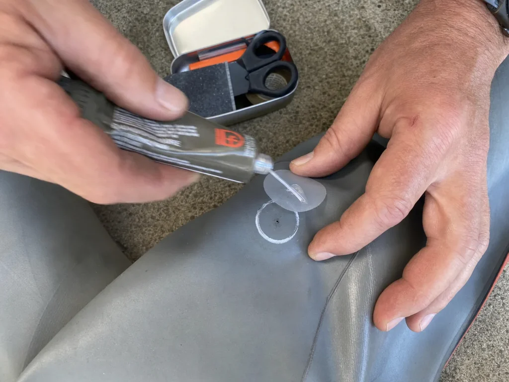 Applying Gear Aid Aquaseal FD adhesive to a marked pinhole patch on a raft