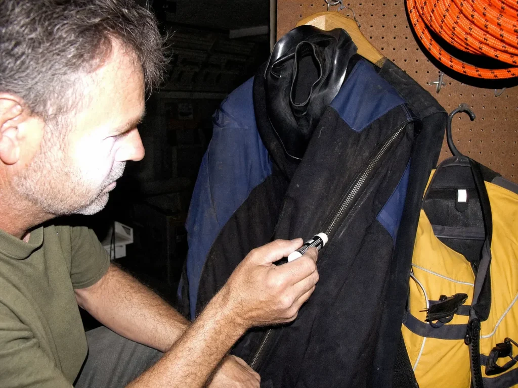 Waxing a drysuit zipper with a McNett Max Wax lube stick in a dim garage