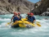 Best Himalayas Rafting Trips: A Rafter’s Data-Backed Guide A team of four diverse and athletic rafters in full gear joyfully paddling through a massive whitewater rapid on a turquoise river in a deep Himalayan gorge.