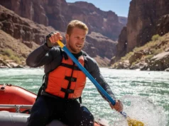 Rafting Gloves Tested for Oar Control & River Safety A man in his early 30s wearing rafting gloves and a life vest, skillfully controlling an oar in the middle of a challenging river rapid.