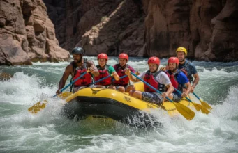 The Definitive Rafting Carnage Guide (Safety & Skills) A group of rafters led by a skilled guide successfully maneuvering their raft through a large and challenging whitewater rapid in a sunny canyon.