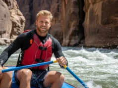 The Essential River Safety Whistle Guide for Rafters A male rafter in a life vest smiles confidently while navigating a rapid, with a safety whistle clearly visible on his shoulder strap.
