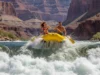 Wave Train Rafting: The Pro’s Guide to Safe Navigation A man and woman in a raft navigate a massive wave train in a vast river canyon, showcasing safe and exciting whitewater rafting.