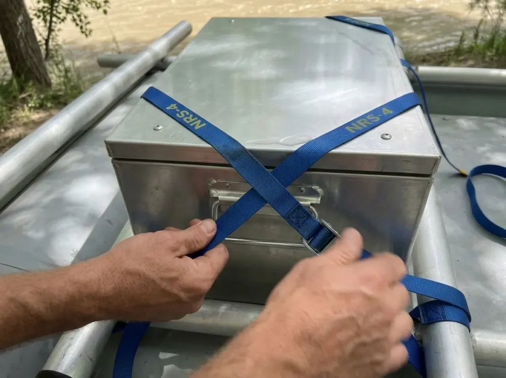Cam straps run in an X-pattern through welded dry box tabs and around the raft frame tube