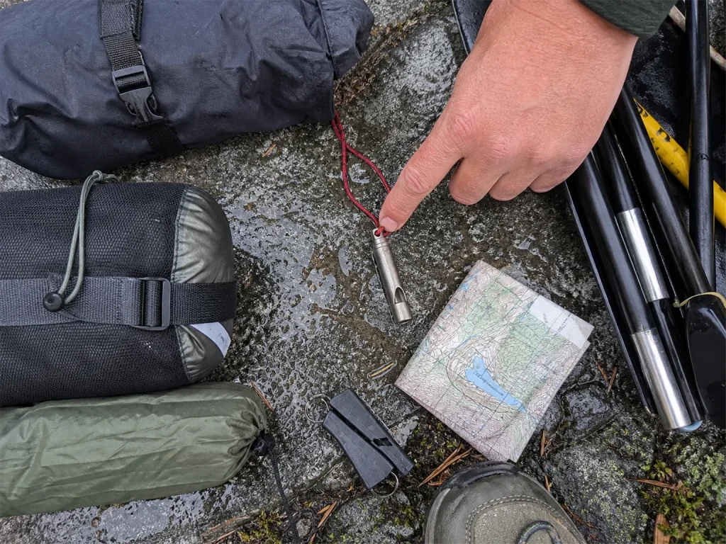 Vargo titanium whistle weighed against a packraft kit laid out on a rock before a run
