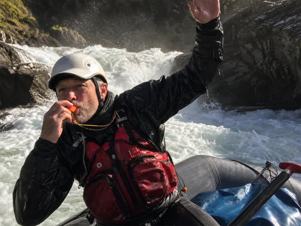 Rafter blowing a Storm safety whistle from an eddy with a loud whitewater rapid behind