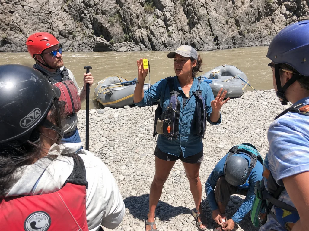 Guide holding up a whistle during a pre-launch safety briefing with a raft crew listening