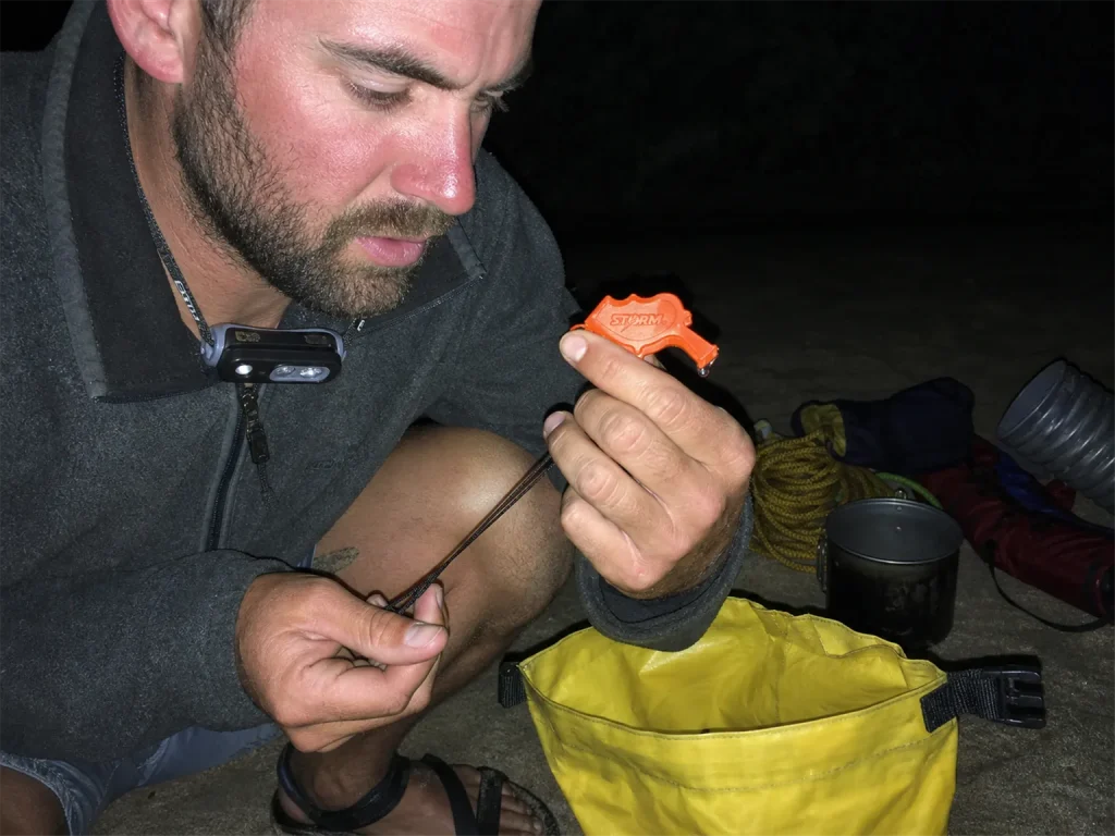 Rafter checking a whistle cord for wear at a river camp on day three of a multi-day trip