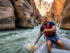 Undercut Rocks Rafting: Spotting & Avoiding River Hazards A male rafter in a life vest skillfully navigates a raft away from a dangerous undercut rock wall in a challenging whitewater river canyon.