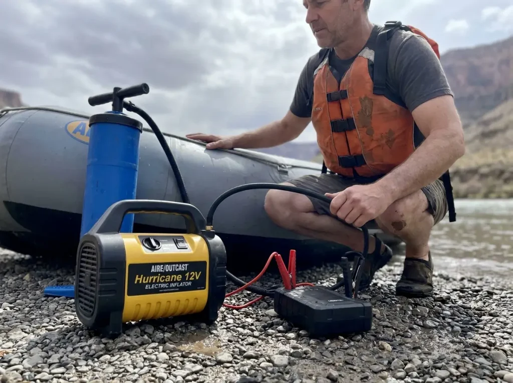 AIRE Outcast Hurricane 12V inflator filling a raft tube with a hand pump waiting nearby