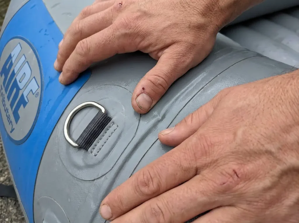 Hands checking the tube seam and D-ring on a budget self-bailing whitewater raft