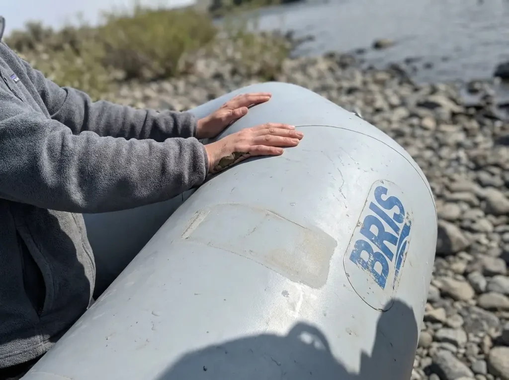 Hands gripping the thick PVC tube of a BRIS inflatable whitewater raft to test its buoyancy and forgiveness