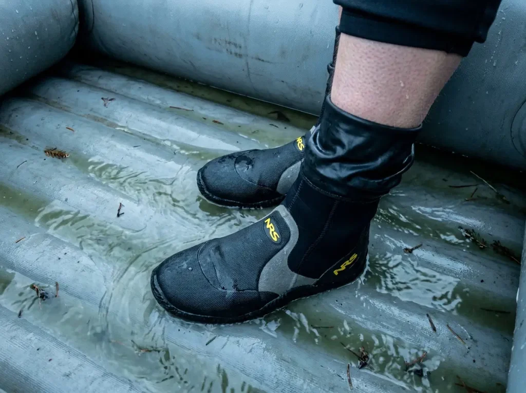 Paddler's feet in wetsuit booties standing in cold ankle-deep water on a self-bailer floor