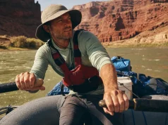 Best Rafting Sun Protection for All-Day River Sun Rafter in a UPF sun hoodie and brimmed hat rowing under bright river-canyon sun