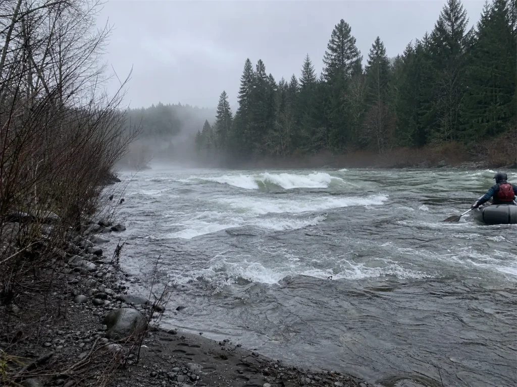 Cold grey whitewater river at dawn showing why cold-water rafting demands a real base layer