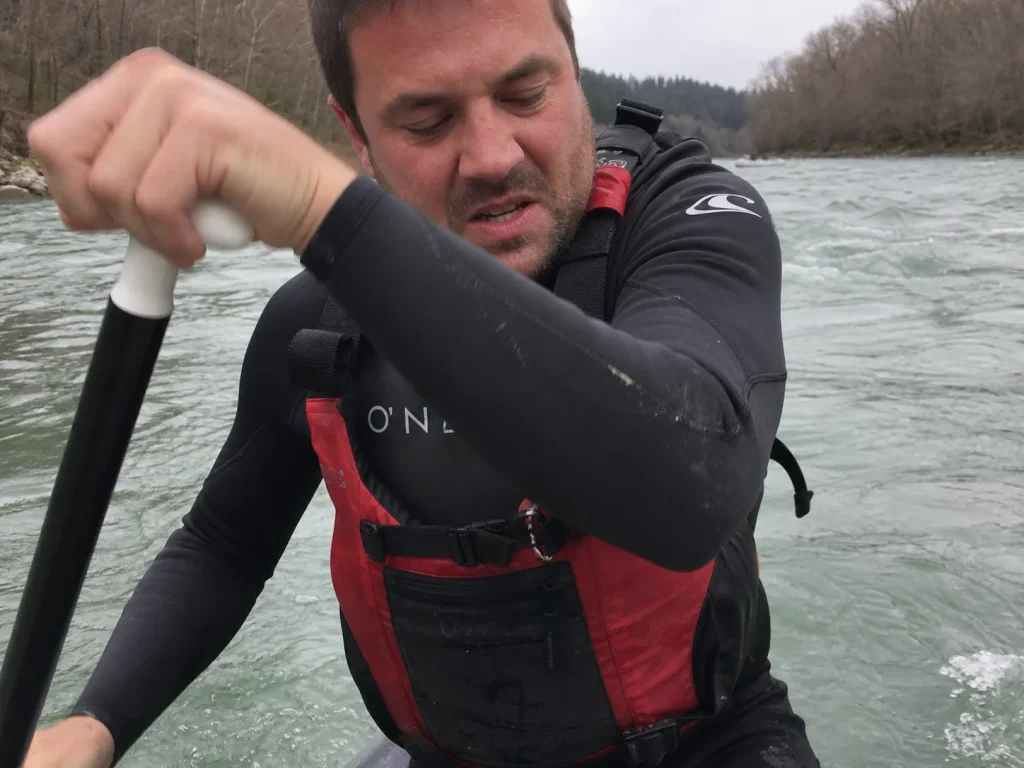 Paddler in a full-sleeve surf wetsuit straining a shoulder mid-stroke showing restricted rotation for rafting