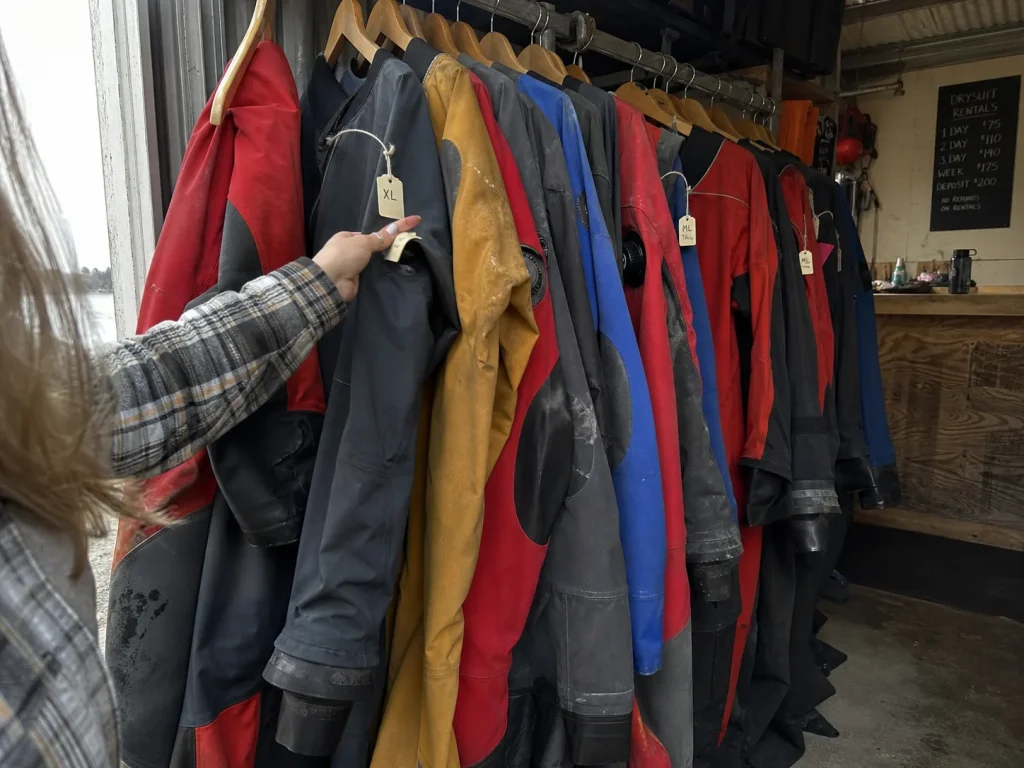 Row of rental drysuits hanging on an outfitter rack, decision between renting and buying