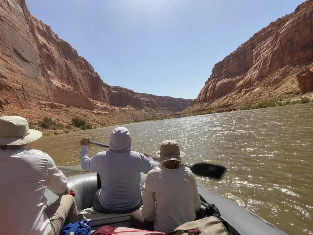Rafters on open sunlit water between reflective canyon walls with no shade