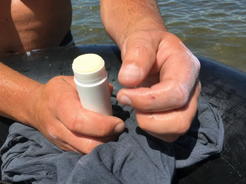 Wet hands holding a mineral sunscreen stick over a soaked cotton shirt on a raft tube