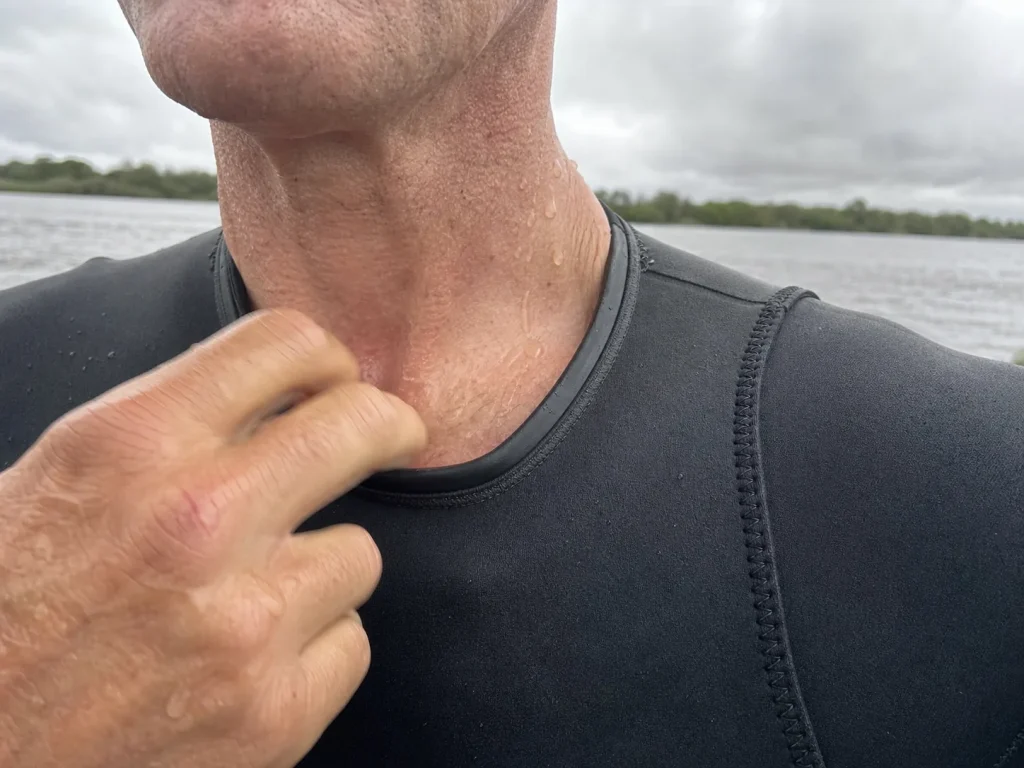 Close-up of a hand checking the neck seal and glued seams on a snug-fitting rafting wetsuit