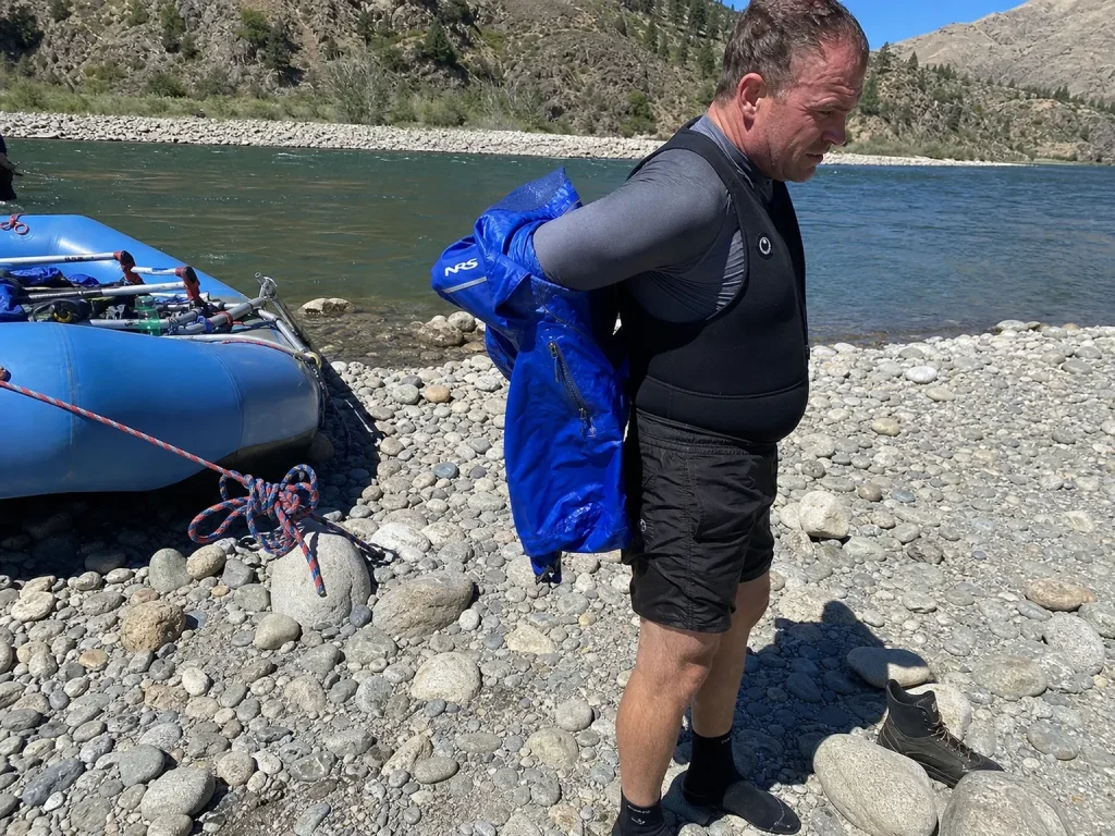 Rafter shedding a paddle jacket layer on a warm afternoon over a wetsuit