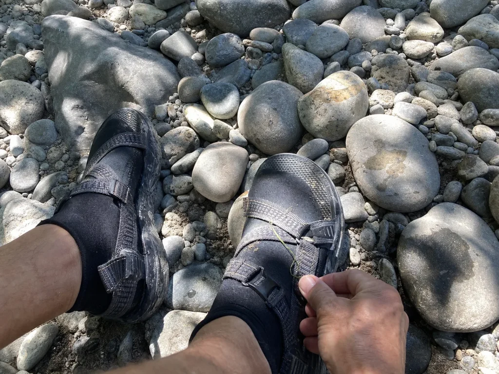 Neoprene sock worn under a strapped river sandal on a gravel bar showing the two-shoe setup