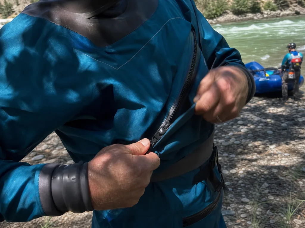 Hands sealing the front-entry zipper and neck gasket on a rafting drysuit at the put-in