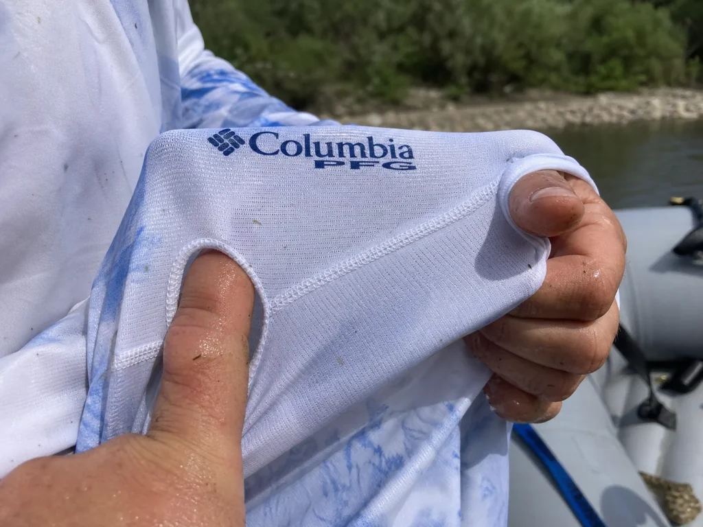 Hands stretching a UPF sun hoodie sleeve to show the dense weave and thumb loop