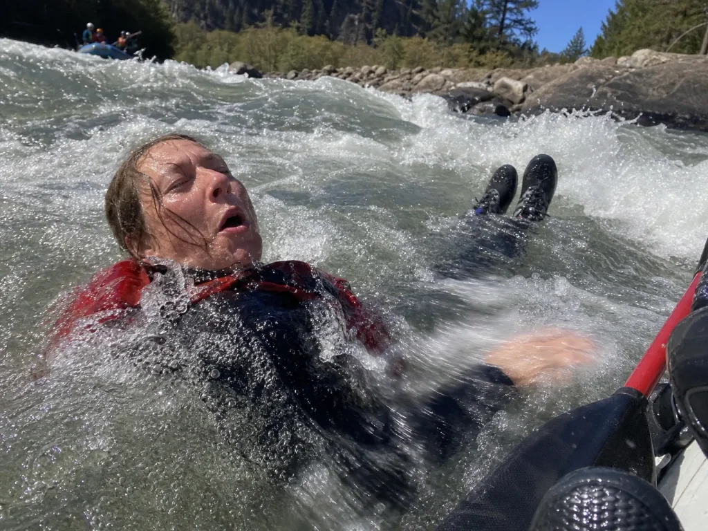 Swimmer in a wetsuit floating feet-up and nose-downstream in cold whitewater during a self-rescue