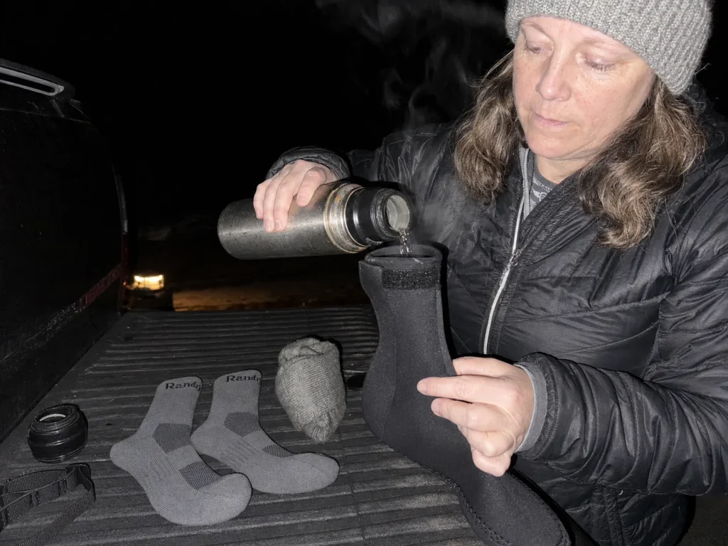 Pre-dawn rafter pouring warm water into a bootie beside waterproof socks and a wool liner
