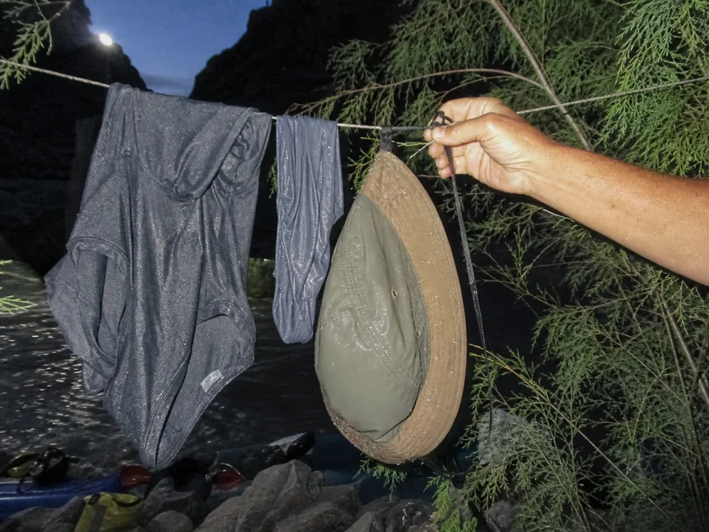 Sun hats and a UPF hoodie hung to dry on a line at a river camp at dusk