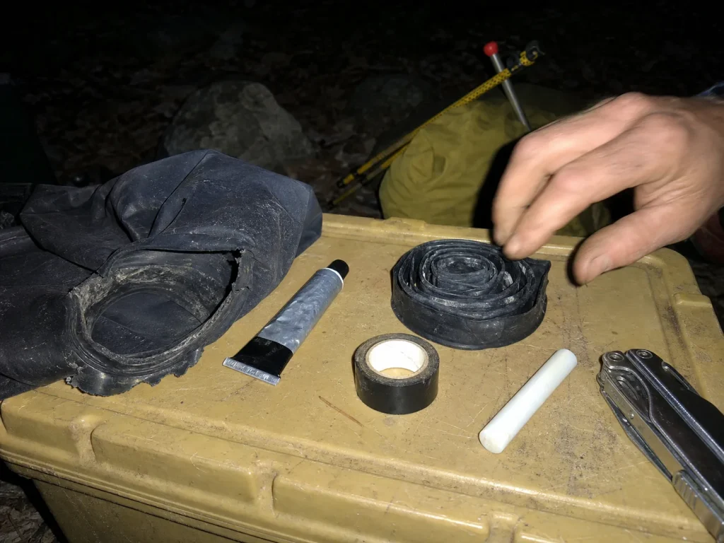 Drysuit field repair kit laid out in camp at dusk with sealant, spare gasket and zipper wax